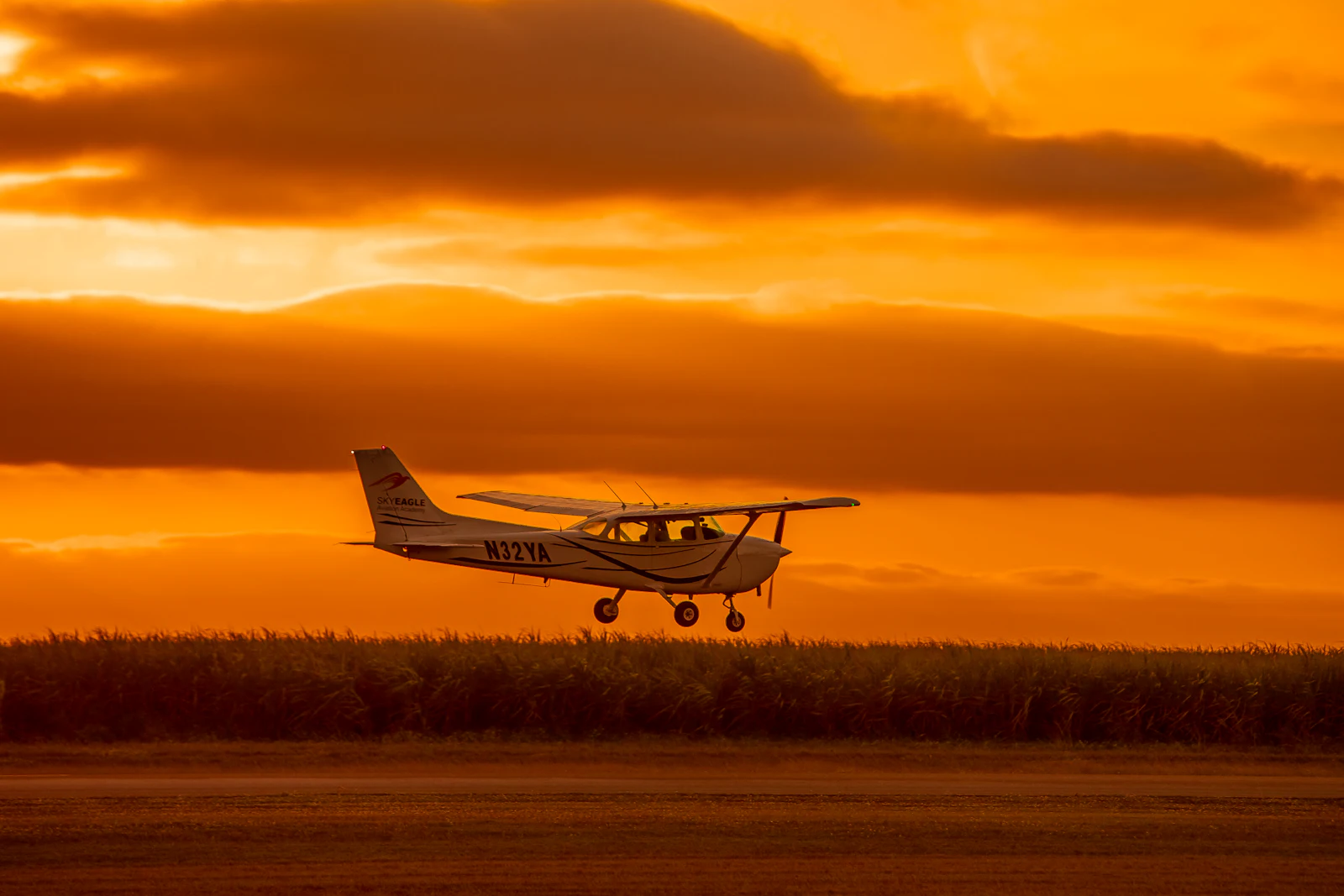 A small airplane flying low over a field at sunset
